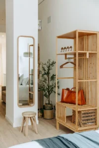Mueble perchero de madera con estantes para maletas, bolso de piel y espejo vertical.