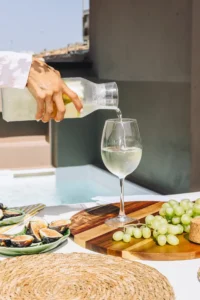 Sirviendo una copa de vino blanco en una mesa de terraza con una tabla de frutas e higos.